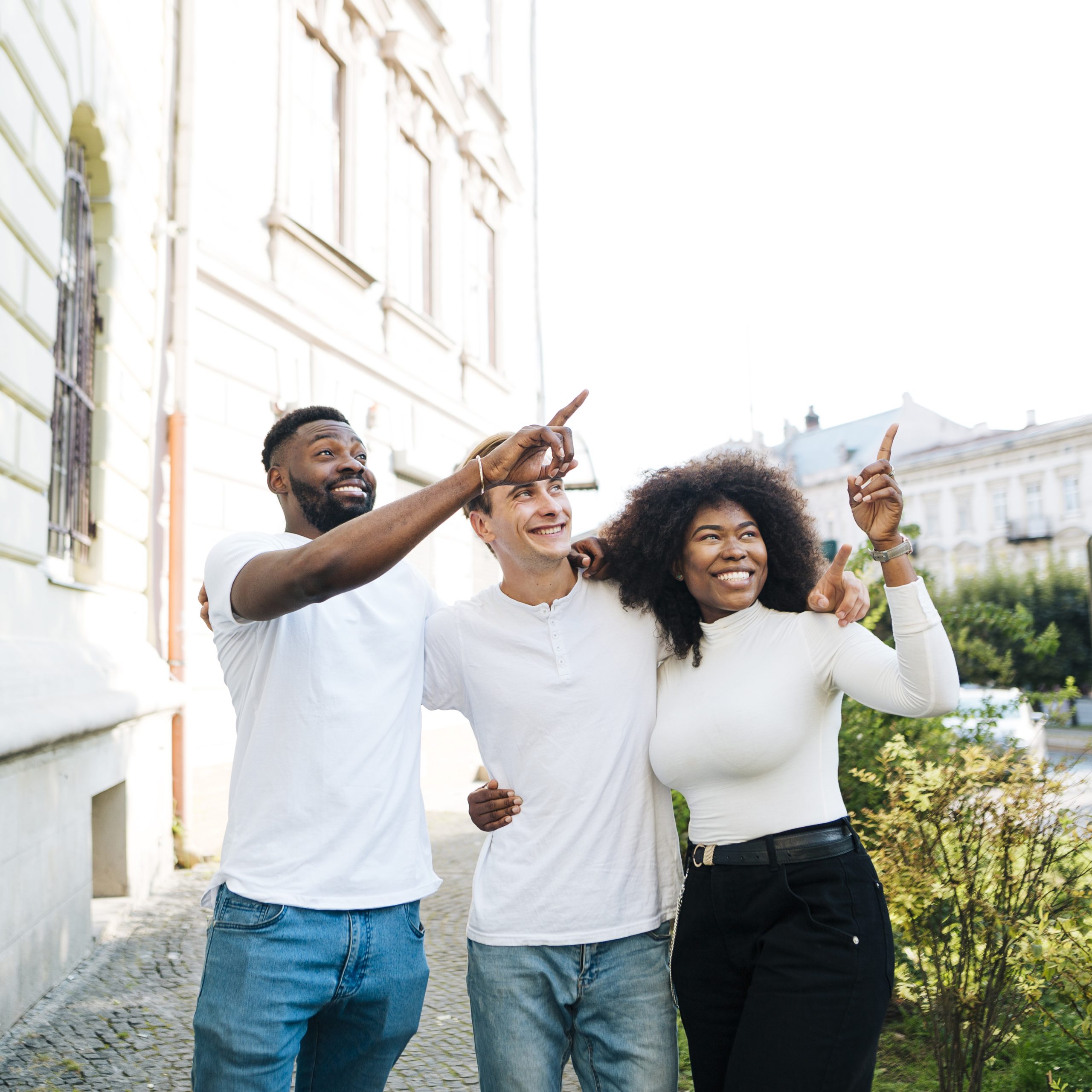 intercultural-friends-hugging-pointing-same-time